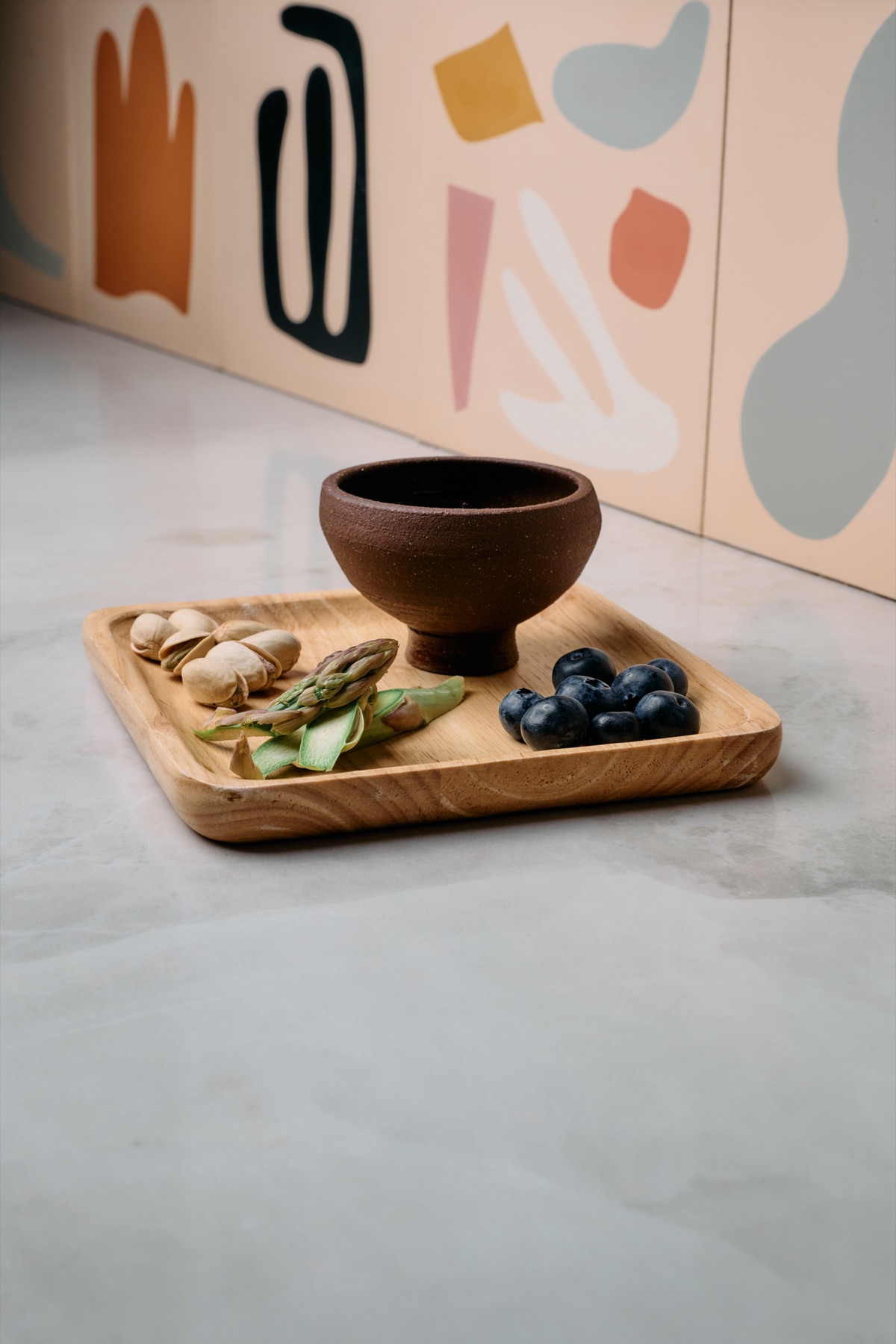 Two copita trays with pistachios, asparagus, and blueberries, colorful mural behind