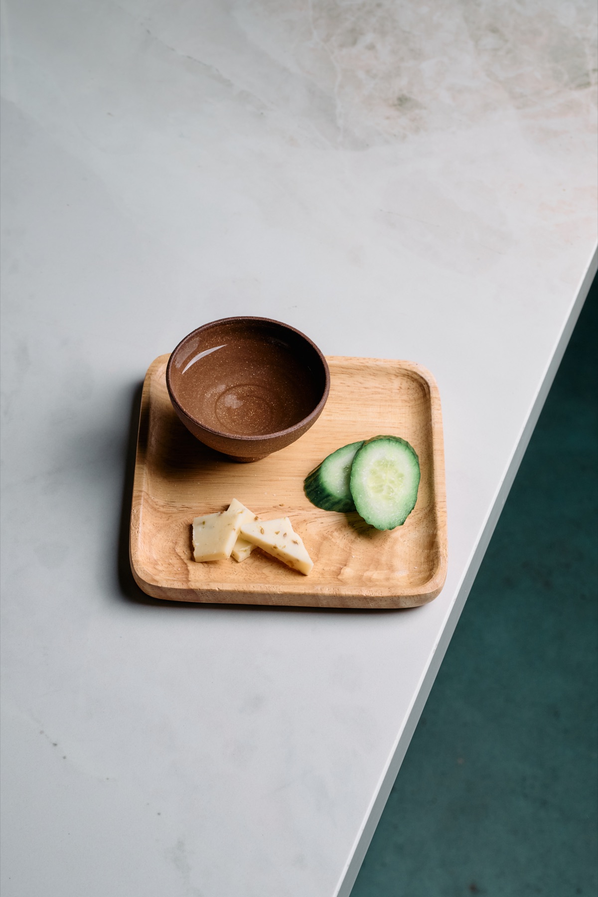 A clay copita and paired nibbles on a wooden tray, marble bar, deep teal behind